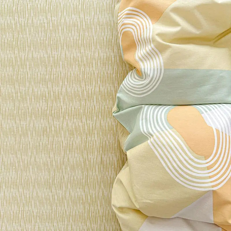 A close-up of a light yellow and sage green cotton duvet cover set with striped detailing.