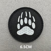 Black embroidered patch featuring a white paw print design on a gray surface.
