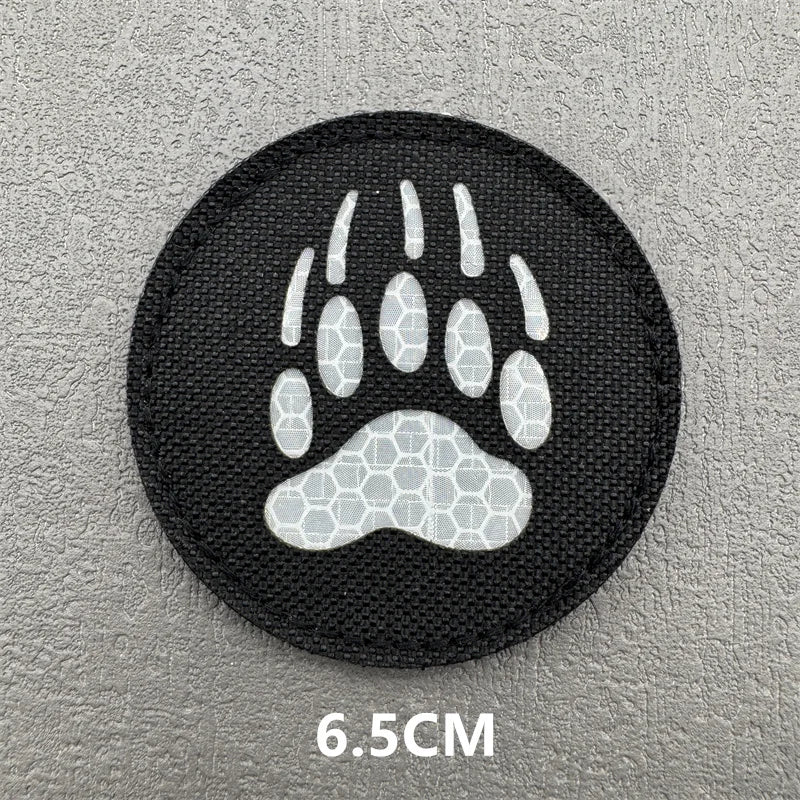 Black embroidered patch featuring a white paw print design on a gray surface.