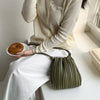 A person wearing a cream-colored top and white pants holds an olive green pleated faux leather crossbody bag.