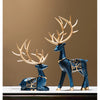 A set of two resin deer figurines with golden antlers and blue bodies displayed on a dark surface.