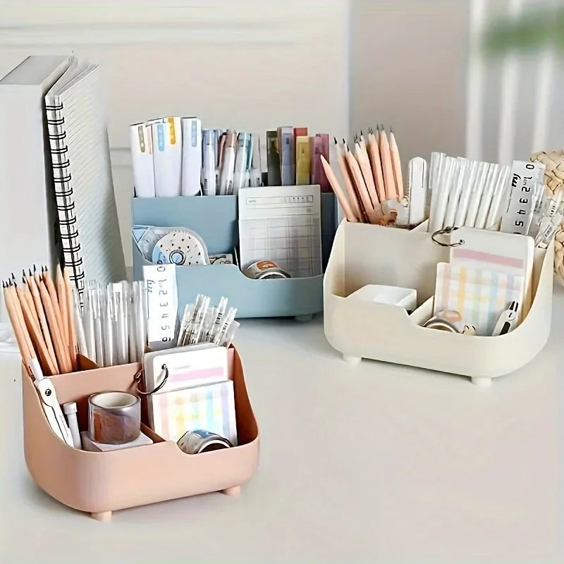 A clear acrylic five-compartment desk organizer filled with pens, pencils, and stationery on a white desk.