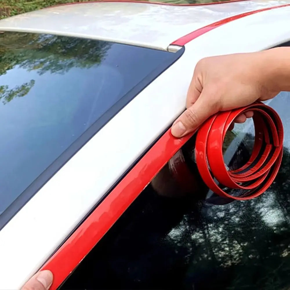 A hand is installing a flexible red PVC car bumper protection strip on the side of a white car.