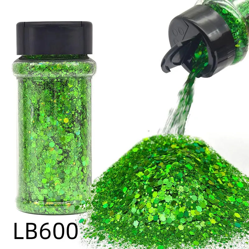 A green holographic chunky nail glitter mix in a jar with a black shaker top and a pile of loose glitter.