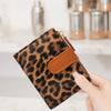 A hand holds a brown leopard print compact zippered wallet with a leather strap and card slots.