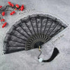 Black lace-trimmed folding fan with a golden edge displayed on a gray surface.