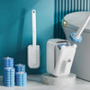 A white wall-mounted disposable toilet brush set with a long handle and replaceable heads is displayed against a teal wall.