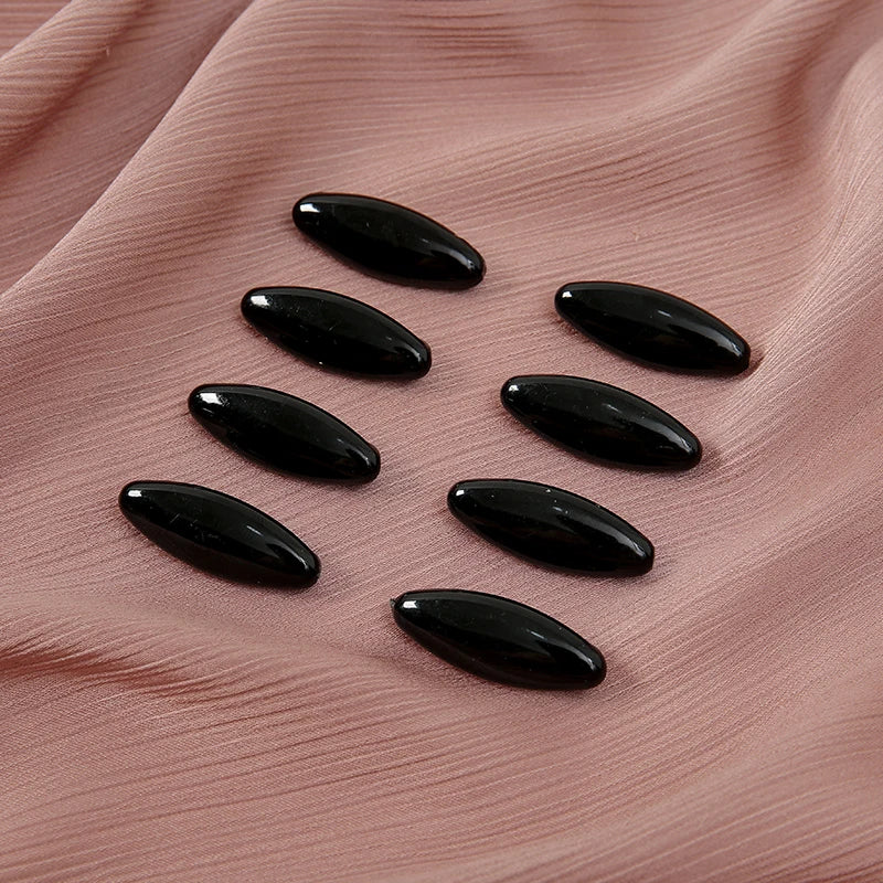 A set of eight black, oval-shaped scarf pins resting on a soft pink fabric.