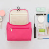 A bright pink waterproof hanging makeup bag with a zipper is shown next to various beauty and grooming tools.