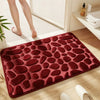 A deep red plush non-slip absorbent bathroom rug with a pebble texture placed on a wooden floor.