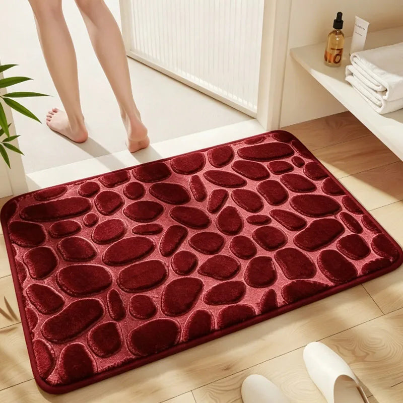 A deep red plush non-slip absorbent bathroom rug with a pebble texture placed on a wooden floor.