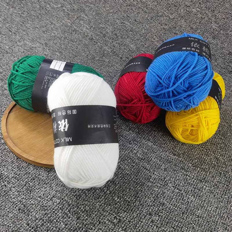 A collection of brightly colored milk cotton yarn skeins in green, red, blue, and yellow are displayed on a gray fabric backg