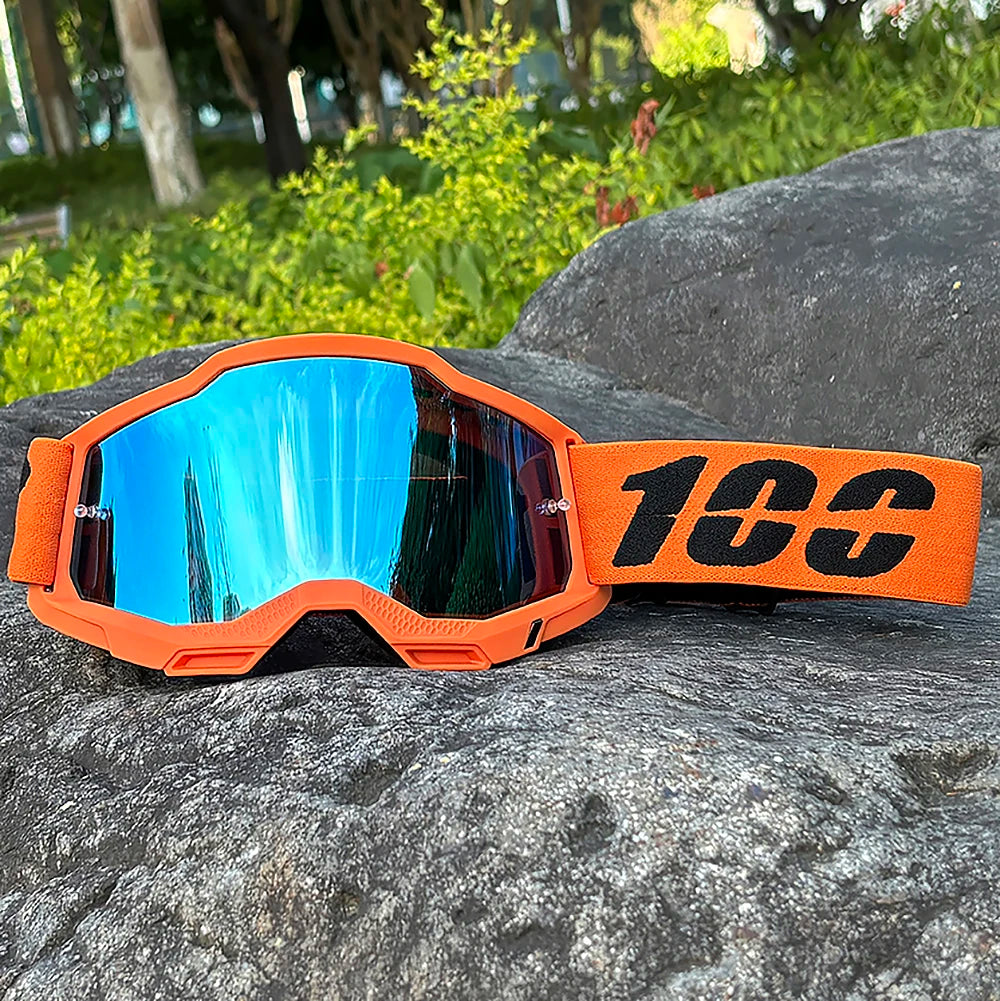 Orange motocross goggles with blue mirrored lenses resting on a dark rock.