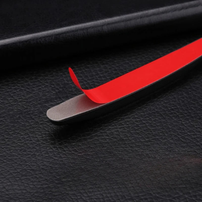 A red car door edge protector strip is shown lying on a black surface.