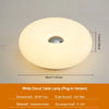 A white donut-shaped plug-in table lamp with a diffused light source.