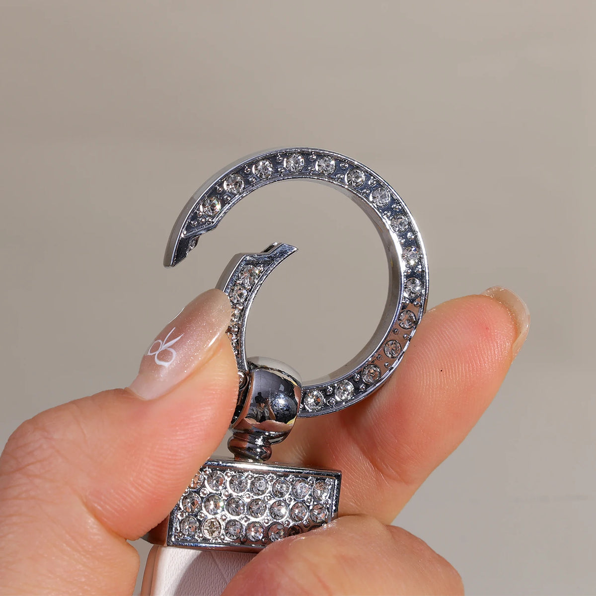 A hand holds a silver O-shaped buckle keychain with a PU leather bow component.