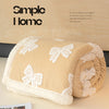 A rolled beige plush jacquard throw blanket with white butterfly patterns is displayed on a light surface.
