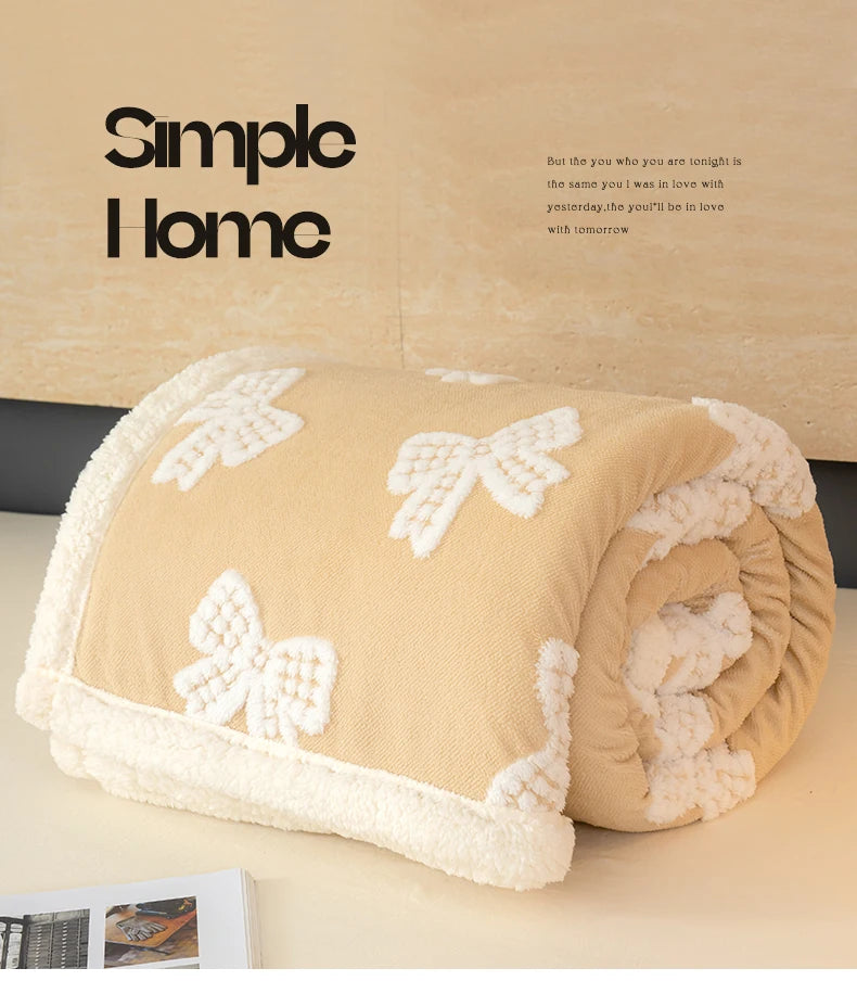 A rolled beige plush jacquard throw blanket with white butterfly patterns is displayed on a light surface.