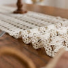 Beige bohemian farmhouse table runner with delicate lace and tassels on a wooden surface.
