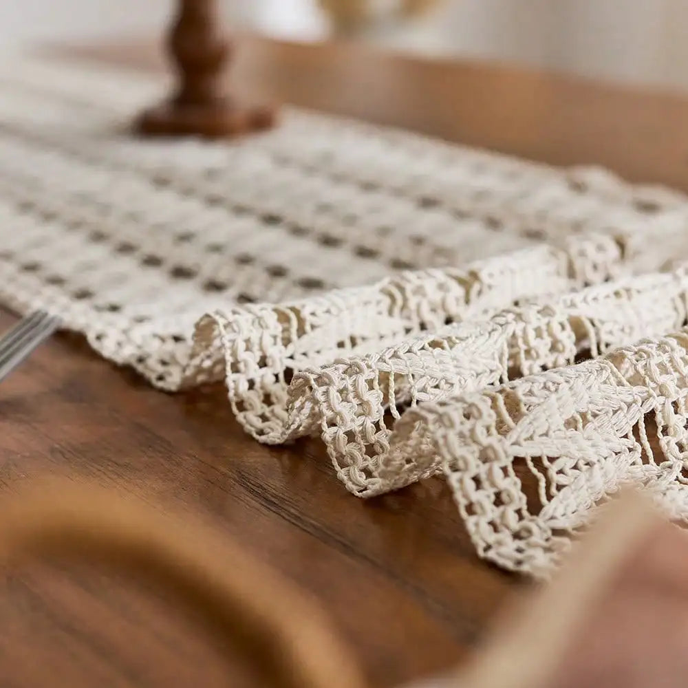 Beige bohemian farmhouse table runner with delicate lace and tassels on a wooden surface.