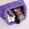 A purple hand-knit clutch bag lined with purple fabric, containing various makeup and beauty items.