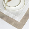 A set of six linen hemstitch napkins displayed on a white table with a ceramic plate and a dried sprig.