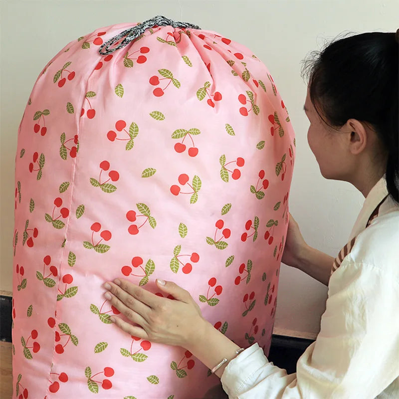 A woman holds a large pink drawstring laundry bag with red and green cherry pattern.