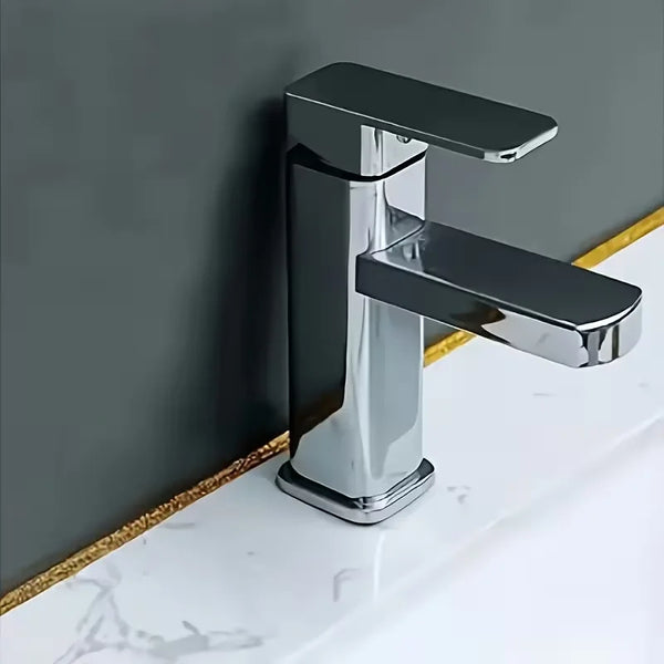 Grifo moderno de cromo montado en una encimera de mármol blanco contra una pared gris.