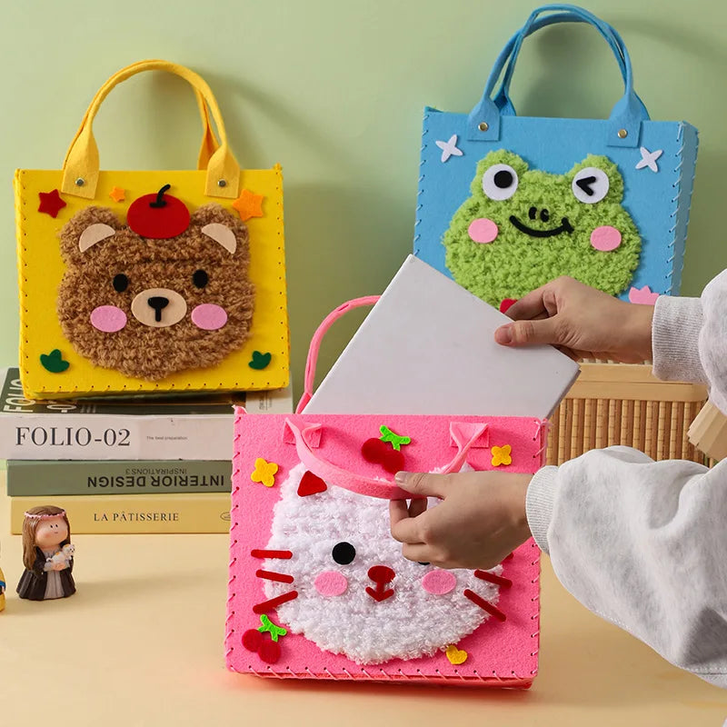 A hand is holding a pink felt pouch with a white cat design, next to blue and yellow felt bags.