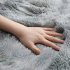 A hand rests on a soft gray plush silk-touch area rug.