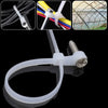 A white reusable screw-hole cable tie with a mounting hole shown alongside various colored and black cables and a wire mesh s