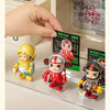 A hand places several collectible dolls, including a yellow and red figure, into a wall-mounted dustproof display case.