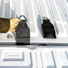 A hand is placing a black fabric bed anchor tie-down into the latch of a truck tailgate.