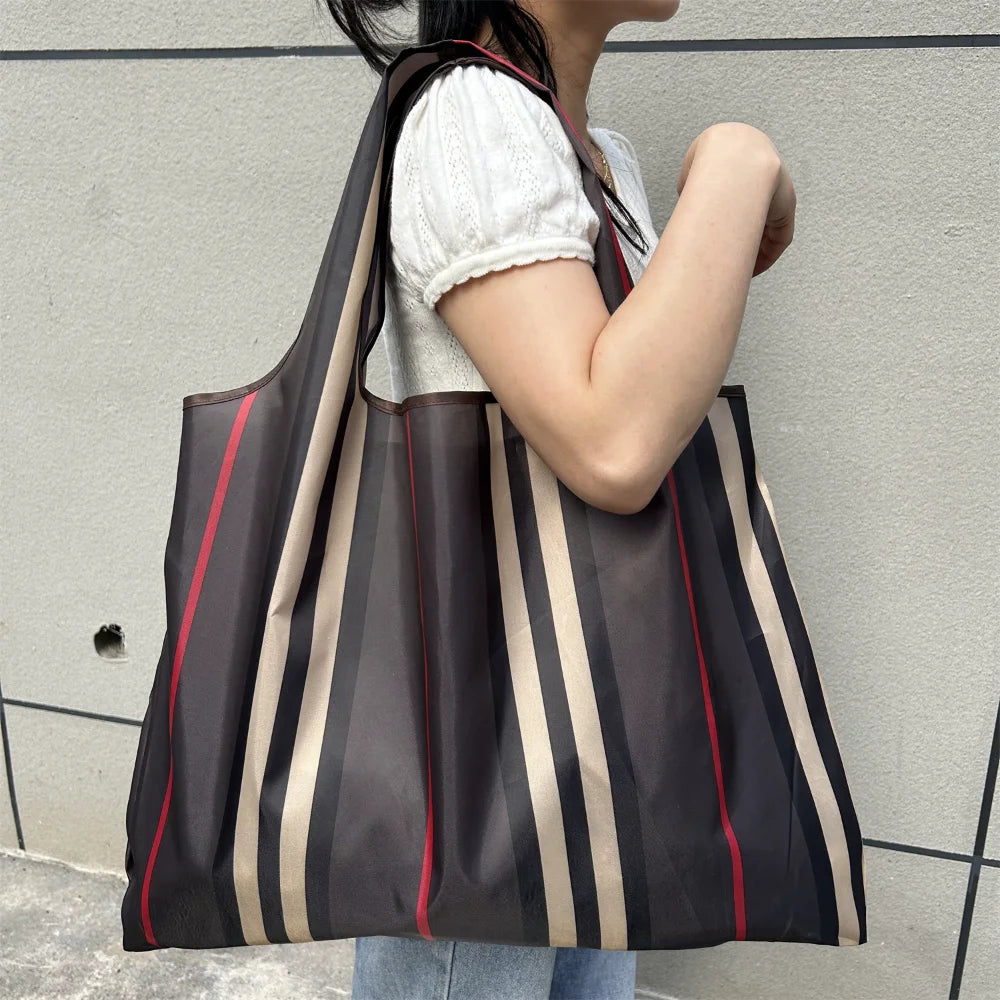 A person is holding a large, striped black and beige fabric tote bag against a light gray wall.