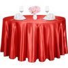 A round red satin tablecloth set for an elegant table with pink flowers and glassware.