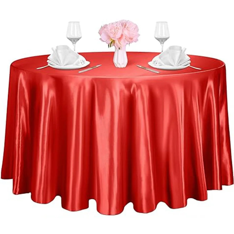 A round red satin tablecloth set for an elegant table with pink flowers and glassware.