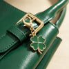 A gold-toned four-leaf clover charm attached to a dark green leather handbag strap.