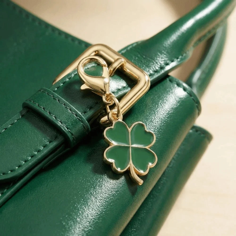 A gold-toned four-leaf clover charm attached to a dark green leather handbag strap.