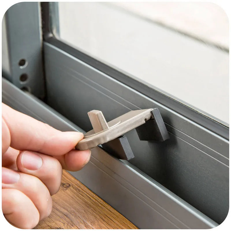 A hand is operating a universal safety window and door lock mechanism on a gray window frame.