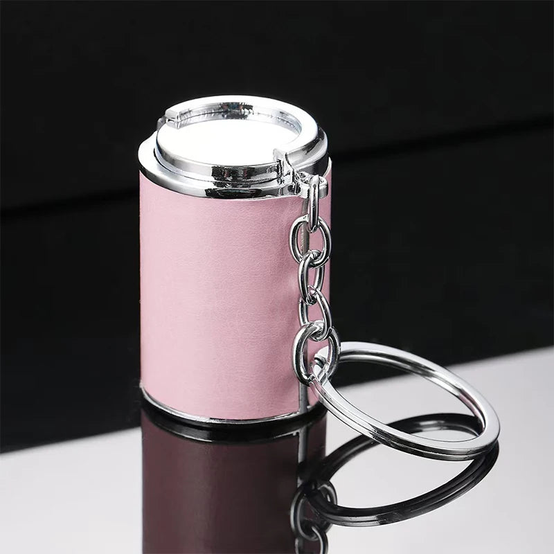 A silver metal coin tube keychain with a clear top is displayed on a reflective surface.