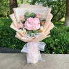 Ein Strauß rosa und gelber Blumen in hellpfirschfarbigem Papier mit grünen Blättern