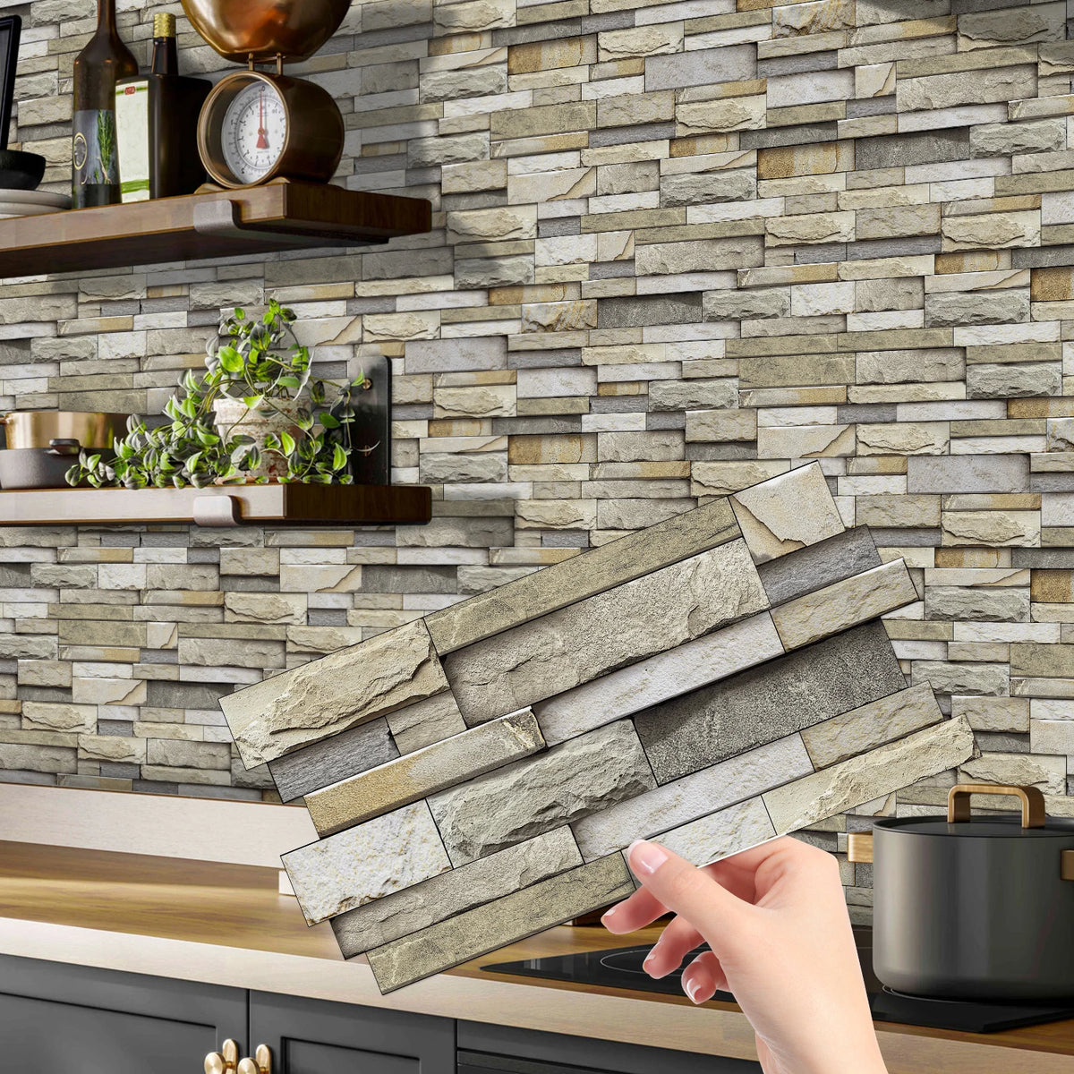 A hand holds a rectangular piece of peel-and-stick tile stickers against a textured stone backsplash.