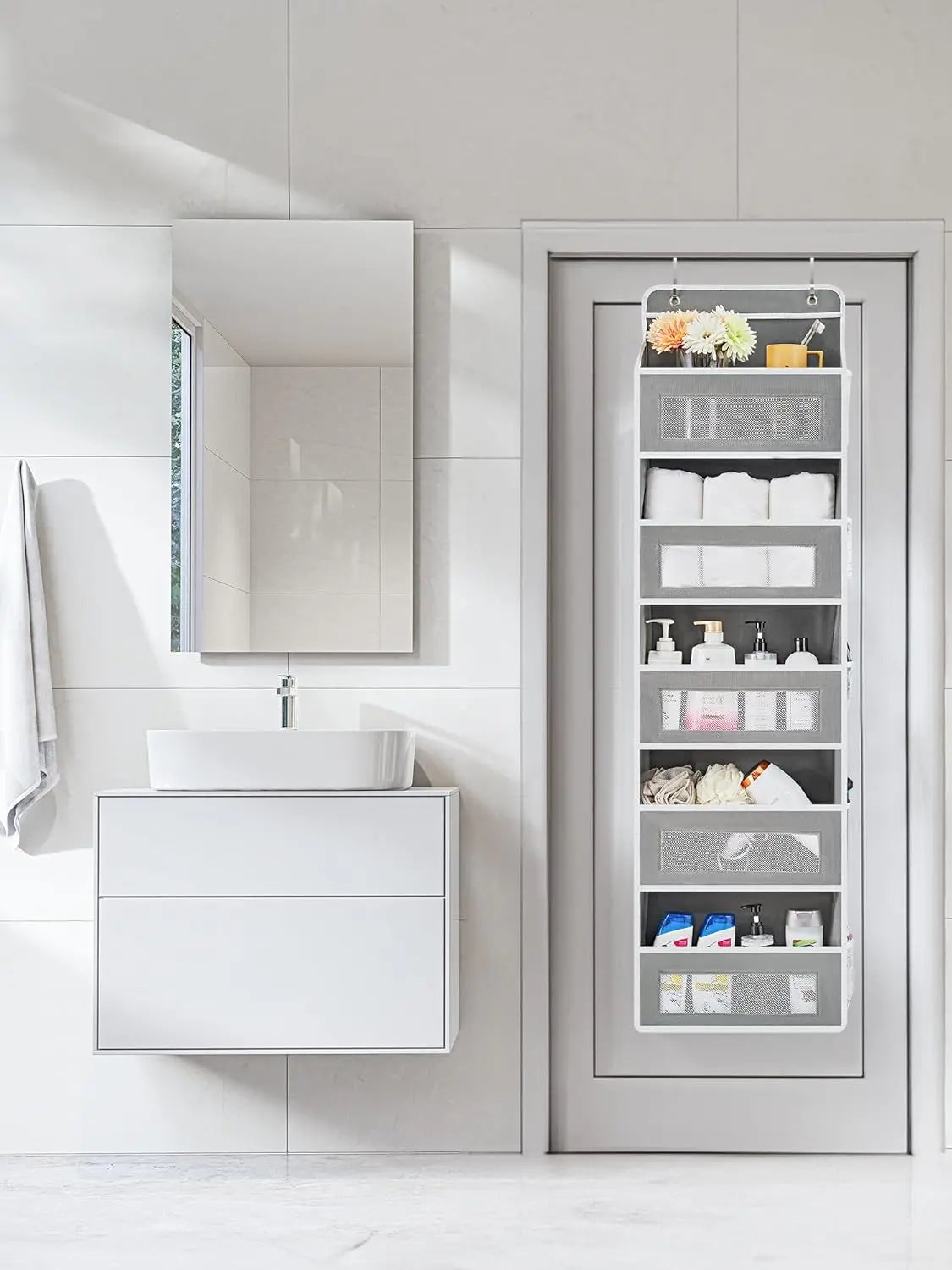 A white over-the-door hanging organizer with five mesh pockets is displayed in a modern bathroom setting.