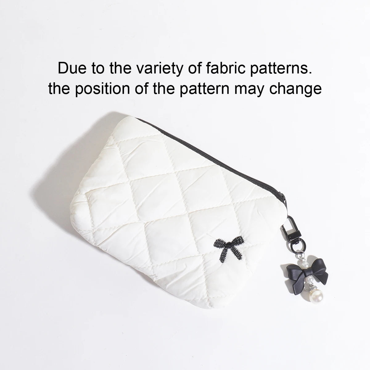 A white quilted makeup bag with a black bow charm is shown against a white background.