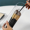 A hand is inserting makeup brushes into a transparent PVC cosmetic bag for waterproof storage.