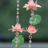 A delicate pink lotus flower pendant featuring a translucent green leaf, suspended on a silver chain.
