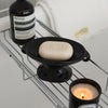 A black ceramic soap dish with an elevated stand holding a light beige bar of soap and a glass candle.