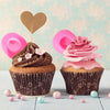 A cupcake decorated with chocolate frosting and topped with a pink heart-shaped cutout and a pink rose swirl.