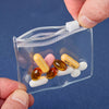 A hand holds a clear plastic organizer bag with a zipper, containing several yellow and pink pills.