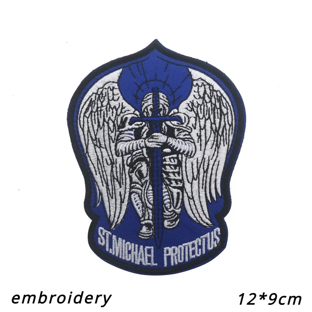 A dark blue patch featuring a silver archangel St. Michael with wings and a halo, embroidered on fabric.